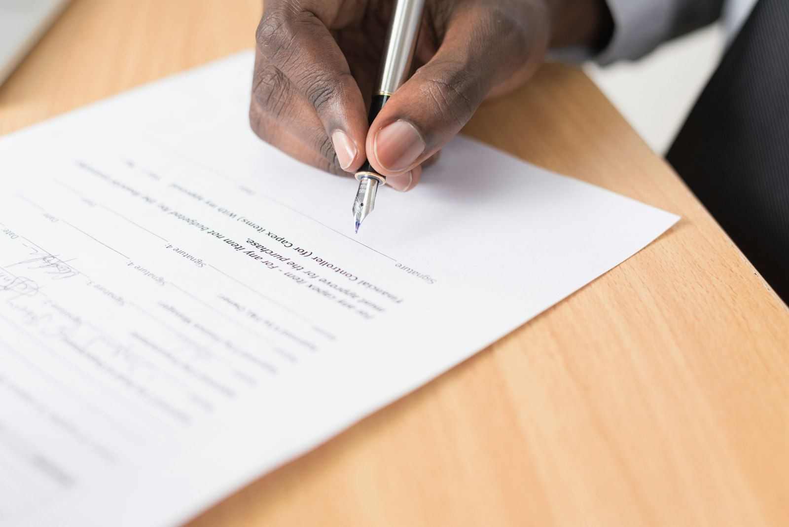 Mano que firma un documento con pluma sobre una mesa